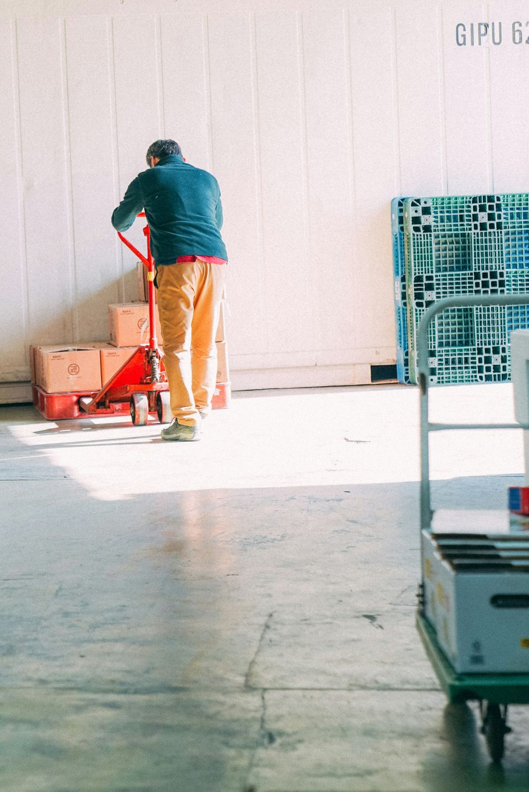 A worker moving cartons on a pallet jack across a bright, clean warehouse floor
