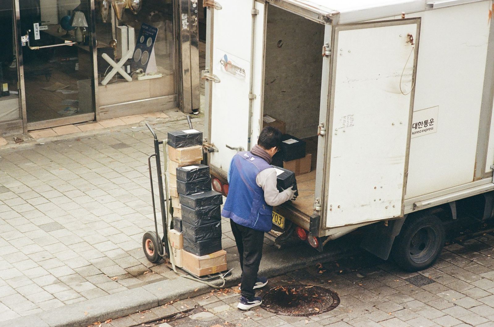 A worker lifting cartons by hand from the back of a small truck onto a hand cart